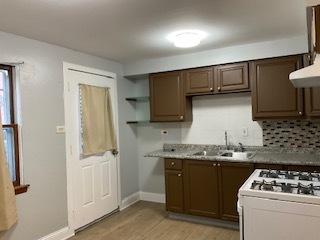 kitchen with dark brown cabinetry, a sink, light wood-style floors, light countertops, and open shelves