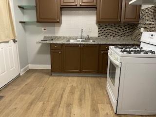 kitchen with open shelves, light wood-style flooring, decorative backsplash, a sink, and white range with gas stovetop