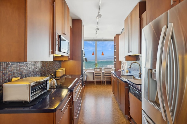 kitchen featuring brown cabinetry, dark countertops, appliances with stainless steel finishes, a water view, and a sink