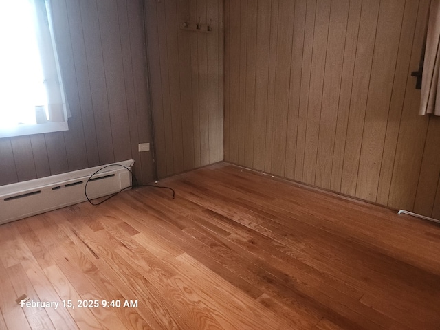 unfurnished room featuring light wood-type flooring, wood walls, and baseboard heating