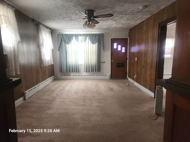 interior space with a baseboard heating unit, light colored carpet, and wooden walls