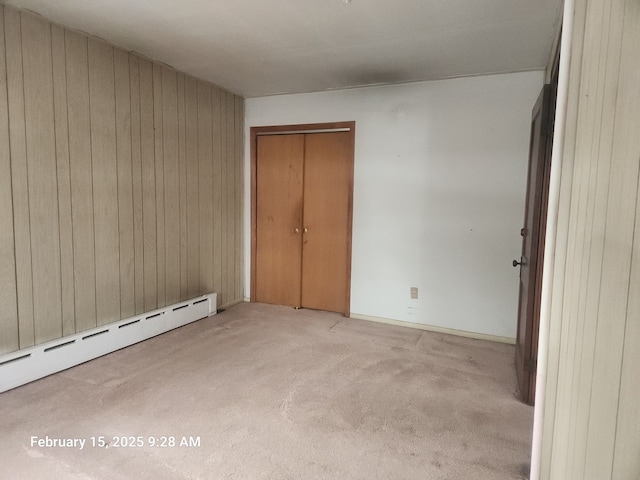 unfurnished bedroom with light carpet, a baseboard radiator, wooden walls, and a closet