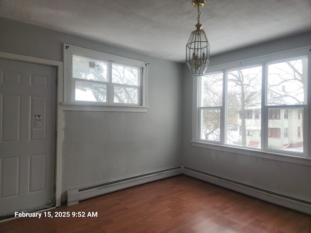 unfurnished room with a notable chandelier, plenty of natural light, baseboard heating, and wood finished floors