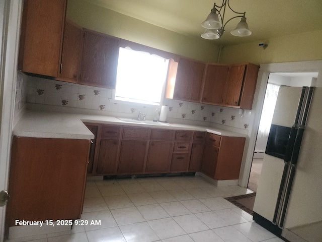 kitchen with a sink, light countertops, hanging light fixtures, freestanding refrigerator, and brown cabinets