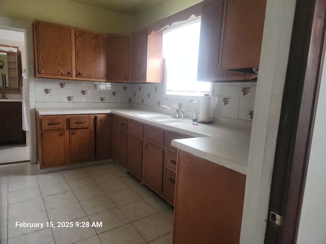 kitchen with light countertops, brown cabinetry, a sink, and backsplash