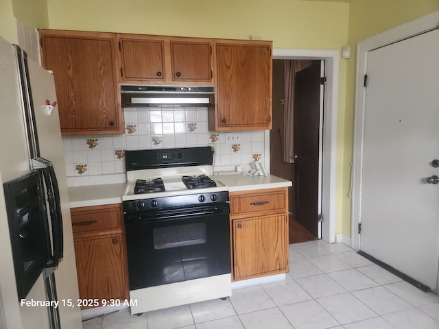 kitchen with brown cabinets, stainless steel refrigerator with ice dispenser, light countertops, black gas stove, and under cabinet range hood