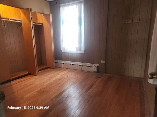 unfurnished bedroom with wood walls, light wood-style flooring, and a baseboard heating unit