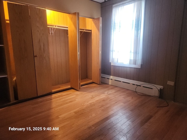 unfurnished bedroom featuring light wood-type flooring, a baseboard radiator, and wooden walls