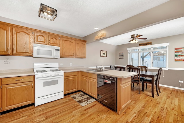 kitchen with white appliances, light wood-style flooring, a peninsula, light countertops, and a sink