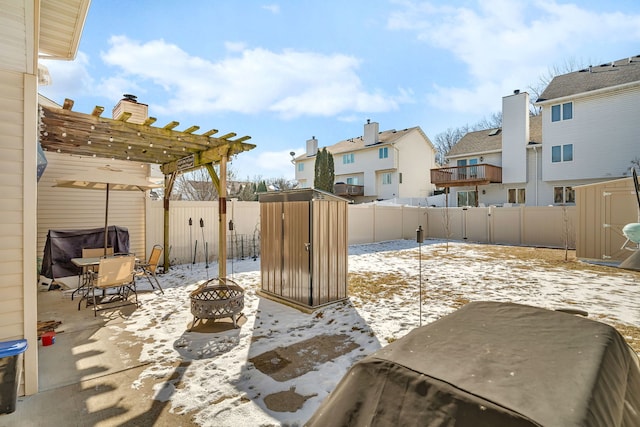 snow covered patio featuring an outdoor fire pit, a fenced backyard, an outdoor structure, a shed, and a pergola