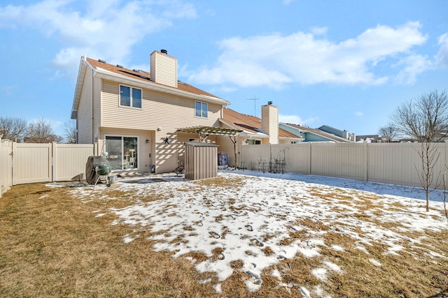 snow covered back of property featuring a chimney, a fenced backyard, and a gate