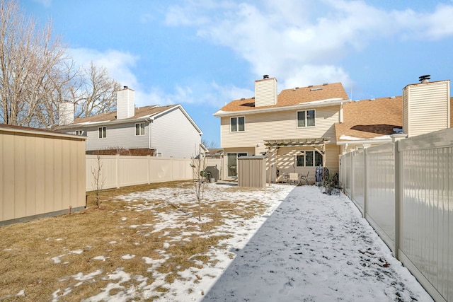 snow covered house with a fenced backyard, a chimney, and a pergola