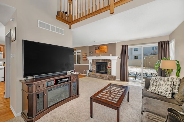 living area featuring light carpet, baseboards, visible vents, a high ceiling, and a fireplace