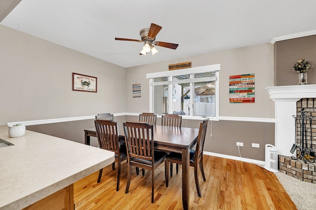 dining room featuring a ceiling fan, a brick fireplace, baseboards, and wood finished floors