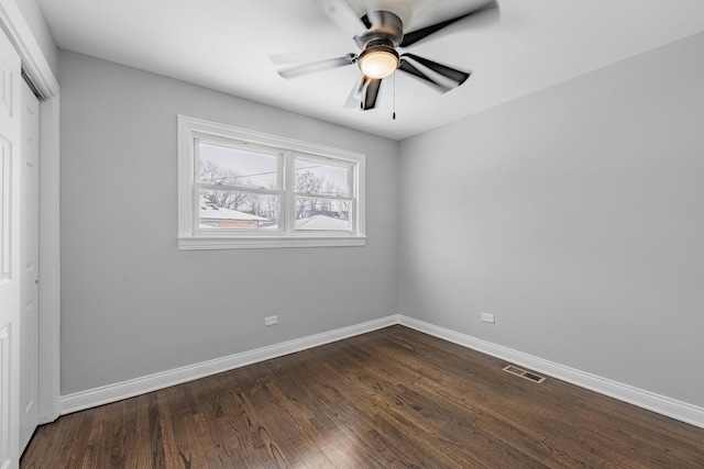 empty room featuring dark wood-style flooring, ceiling fan, visible vents, and baseboards