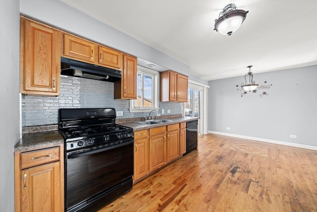 kitchen featuring dark countertops, light wood-style floors, a sink, under cabinet range hood, and black appliances