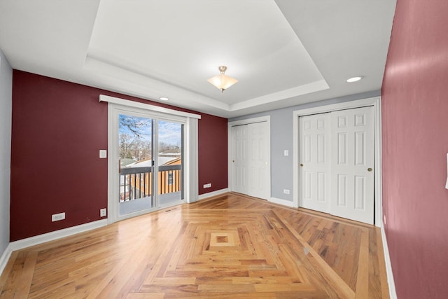 unfurnished bedroom with access to outside, a tray ceiling, two closets, and baseboards