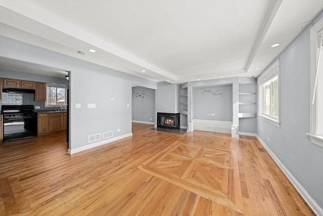 unfurnished living room featuring a lit fireplace, a wealth of natural light, and baseboards