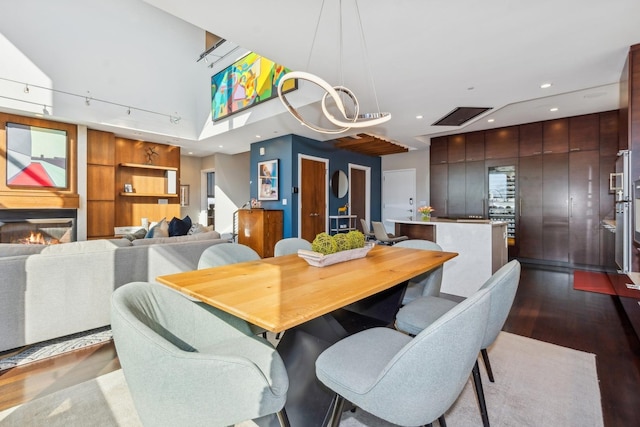 dining space featuring recessed lighting, a high ceiling, wood finished floors, a glass covered fireplace, and track lighting