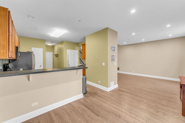 kitchen featuring baseboards, appliances with stainless steel finishes, dark countertops, light wood-style floors, and brown cabinetry