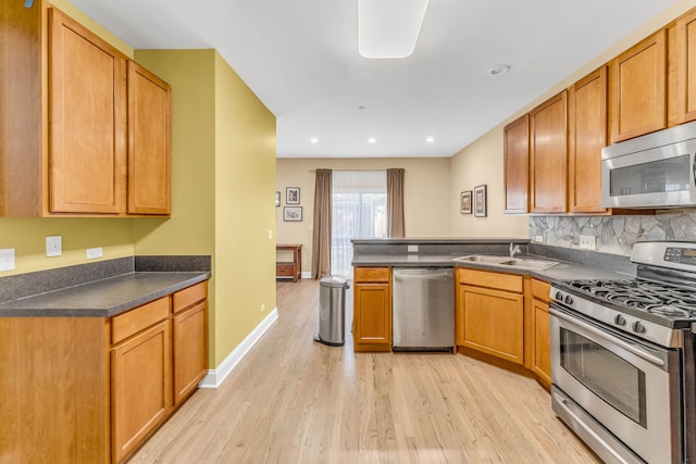 kitchen with light wood-style floors, a peninsula, appliances with stainless steel finishes, a sink, and dark countertops