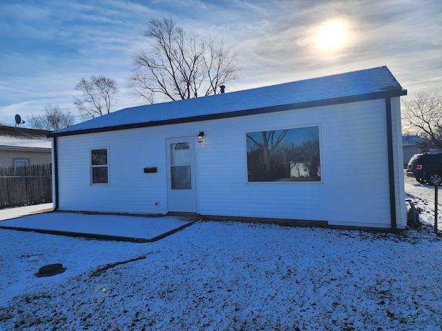 snow covered back of property featuring a patio and fence