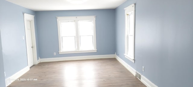 spare room featuring light wood-type flooring, visible vents, and baseboards