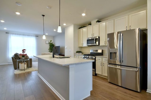 kitchen with a center island with sink, hanging light fixtures, appliances with stainless steel finishes, open floor plan, and white cabinets