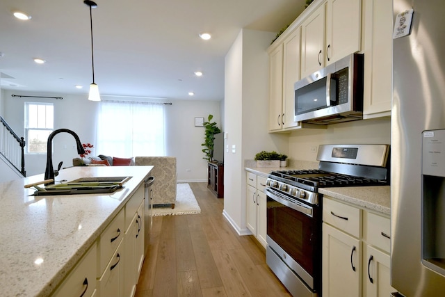 kitchen with decorative light fixtures, stainless steel appliances, light wood-style floors, a sink, and light stone countertops