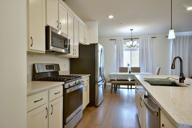 kitchen with light stone counters, stainless steel appliances, hanging light fixtures, white cabinetry, and a sink