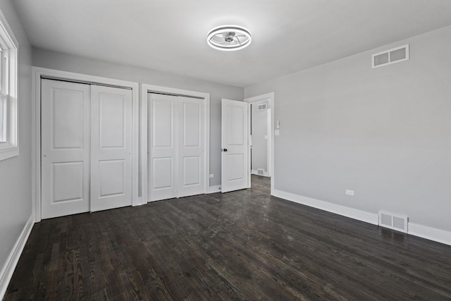 unfurnished bedroom with dark wood-style flooring, two closets, visible vents, and baseboards