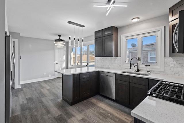 kitchen featuring decorative backsplash, dark wood-type flooring, a peninsula, stainless steel appliances, and a sink