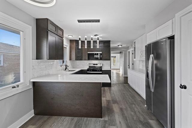 kitchen featuring stainless steel appliances, tasteful backsplash, light countertops, a sink, and a peninsula