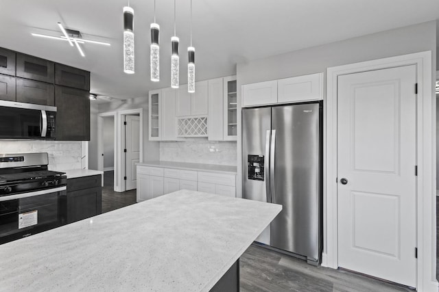 kitchen with dark wood-type flooring, glass insert cabinets, stainless steel appliances, and decorative backsplash