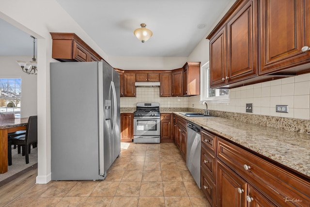 kitchen featuring stainless steel appliances, light stone counters, backsplash, and under cabinet range hood