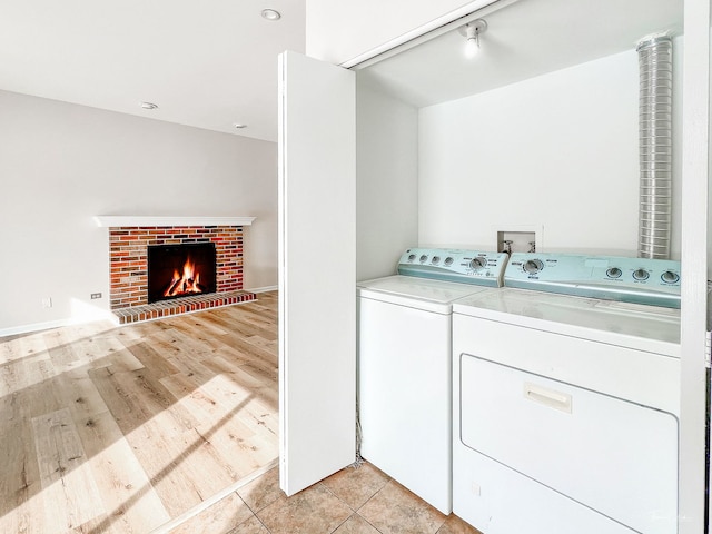 laundry room with laundry area, light wood-type flooring, a brick fireplace, and washer and dryer