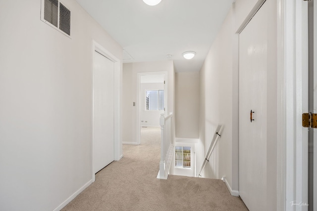 hallway with light colored carpet, baseboards, visible vents, and an upstairs landing