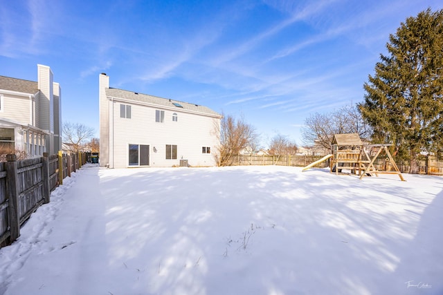 snow covered property with a fenced backyard, a chimney, and a playground