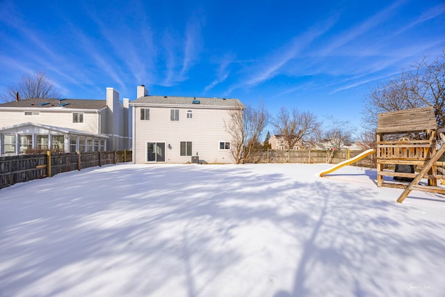 snow covered house with a playground and a fenced backyard