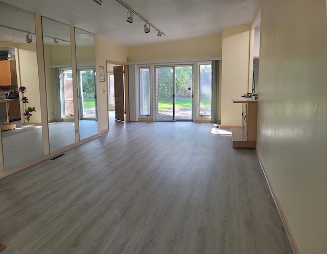 unfurnished living room featuring baseboards, visible vents, track lighting, and wood finished floors