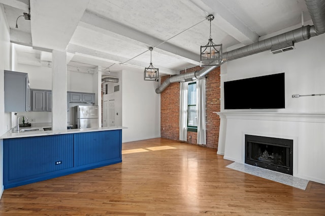 unfurnished living room featuring a high ceiling, a fireplace with flush hearth, a sink, brick wall, and wood finished floors