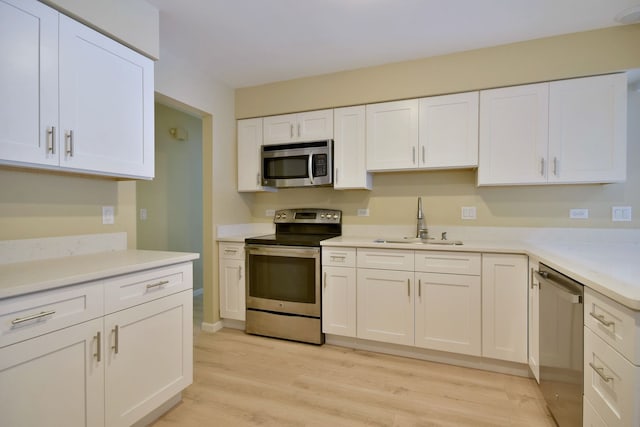 kitchen with light countertops, appliances with stainless steel finishes, white cabinets, a sink, and light wood-type flooring