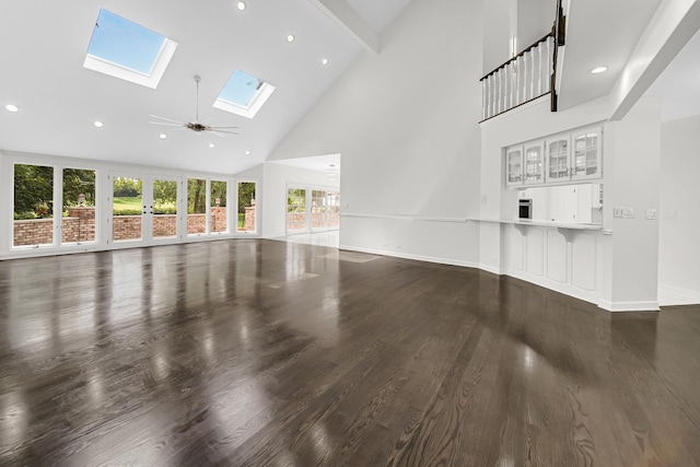 unfurnished living room featuring a skylight, recessed lighting, dark wood-type flooring, high vaulted ceiling, and baseboards