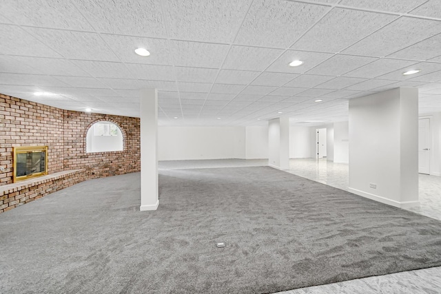 finished basement featuring a paneled ceiling, carpet flooring, a fireplace, and brick wall