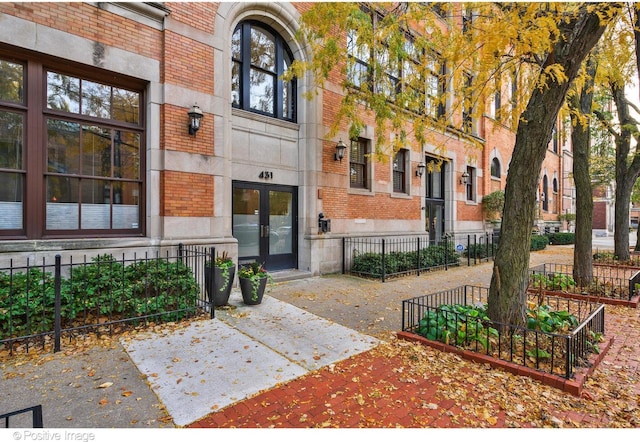 doorway to property featuring fence, french doors, and brick siding