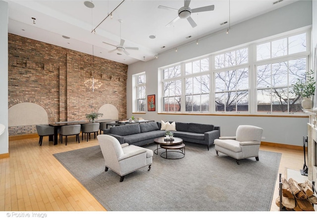 living room featuring a ceiling fan, a high ceiling, brick wall, and wood finished floors