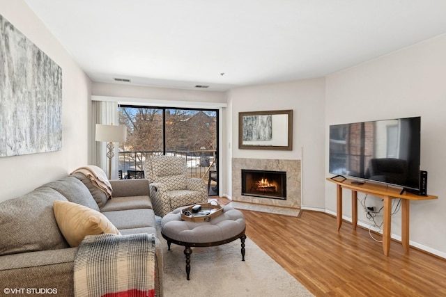 living room with a high end fireplace, visible vents, baseboards, and wood finished floors