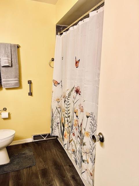 bathroom with baseboards, visible vents, toilet, and wood finished floors