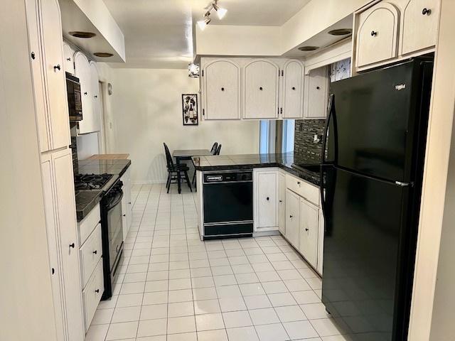 kitchen with dark countertops, white cabinetry, light tile patterned flooring, a peninsula, and black appliances