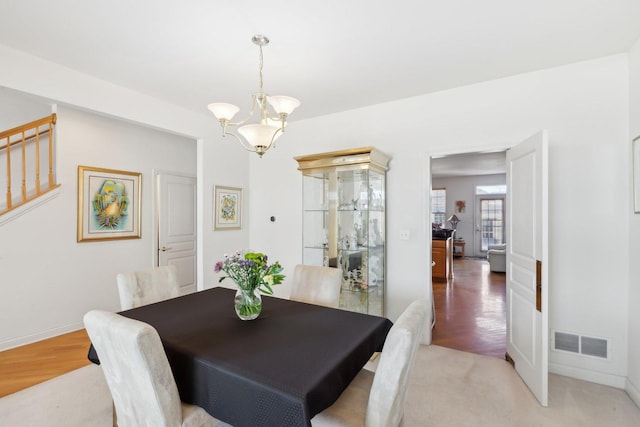 dining space with baseboards, visible vents, wood finished floors, an inviting chandelier, and stairs